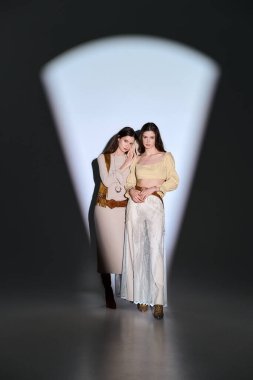 İkiz kardeşler şık kıyafetler içinde şık bir şekilde dururlar, odaklanmış ışıkta güzelce yakalanırlar..