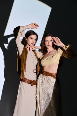 İkiz kardeşler dramatik bir arkaplan karşısında şık kıyafetler giyerler..