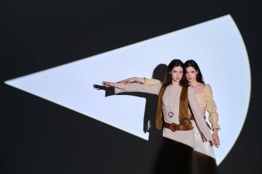 İki güzel ikiz kardeş, kendine güvenen şık kıyafetler ve eşsiz ışıklandırmayla poz verirler..