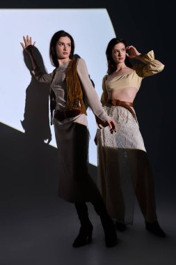 Moda kıyafetleri içindeki iki genç kız kardeş sanatsal bir şekilde çarpıcı bir ışık arka planına karşı poz veriyor..