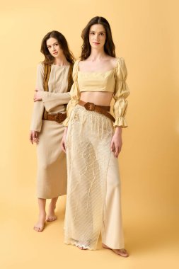 İkiz kız kardeşler şık kıyafetler içinde, ışık saçan bir stil ve zarafetle parlak bir arkaplan karşısında poz verirler..