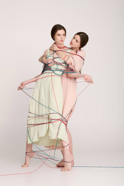 Two stylish twin sisters demonstrate their close relationship while wrapped in colorful strings.