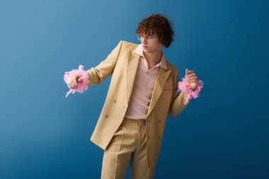 Genç bir çocuk, kendine has tarzını, modaya uygun kıyafetleriyle mavi bir zemine karşı oynak hareketleriyle sergiliyor..