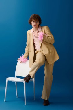 Genç çocuk kendine güvenen bir duruş sergiliyor. Pembe aksanlı, modaya uygun bej bir elbise giyiyor. Gençlik enerjisi yayıyor..