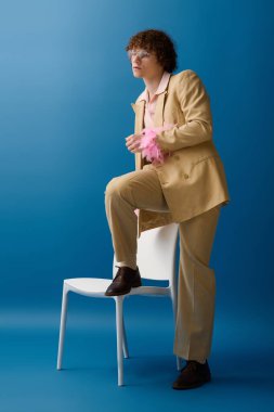 Şık bir çocuk, şık kıyafetlerini ve oyuncu aksesuarlarını vurgulayarak kendine güvenen bir şekilde sandalyede poz verir..