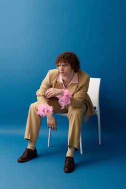 Delikanlı, modaya uygun kıyafetinin altını çizerken, aynı zamanda eğlenceli aksesuarlarla mavi bir zemine oturuyor..