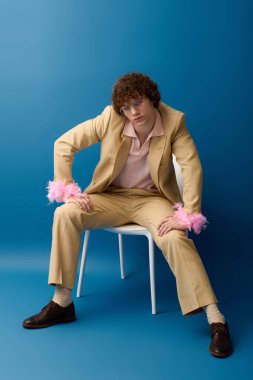 Şık bir genç kendine güvenen bir poz veriyor. Parlak mavi bir arkaplan karşısında modaya uygun kıyafetler giyiyor..