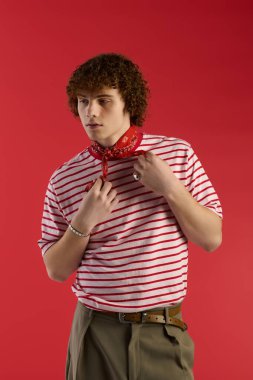 Bir çocuk kırmızı arka plana karşı şık kıyafetler içinde poz veriyor, kendine güveni tam..