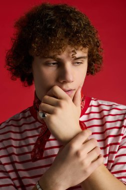 Genç çocuk, özgünlüğünü kırmızı bir arka plana karşı şık bir kıyafetle ifade ediyor..