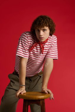 Bir çocuk, gençlik enerjisi saçarak, bir tabureye yaslanırken, modaya uygun bir şekilde poz verir..