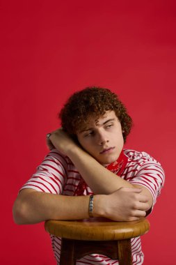 Genç çocuk modaya uygun giyiniyor, rahat bir poz veriyor düşünceli bir ifadeyle, tam bir tarz sahibi..