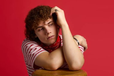 Genç bir çocuk kollarını dinlendirirken, şık kıyafetler giyerken ve tarzını sergilerken kendine güvenen bir poz verir..