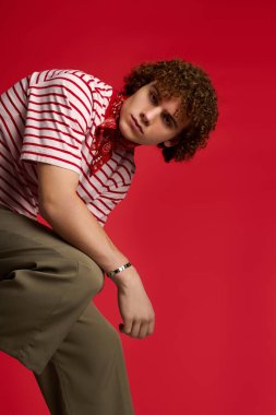 Şık bir genç cesur bir kırmızı arka plana karşı özgüvenli bir duruş sergiliyor. Yetenek ve enerji saçıyor..