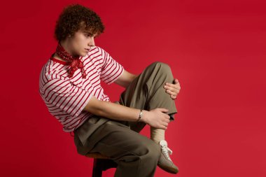 Gençler bir taburede güven içinde poz veriyor, gösterişli bir moda ile cesur bir arka plana karşı..