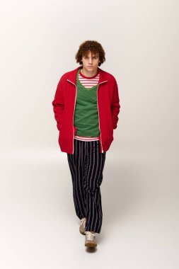 Şık giyinen genç dinamik bir duruş sergiliyor, moda kıyafetleri ve canlı renkleri vurguluyor.