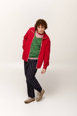 Genç bir çocuk, kırmızı ceket ve çizgili pantolonlu modaya uygun bir şekilde poz veriyor..