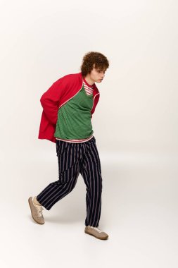 Şık giyinmiş genç bir çocuk enerjik bir şekilde yürüyor, eşsiz moda seçimleriyle hava atıyor..