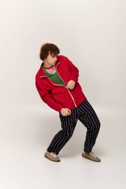 Cesur renkler giymiş şık bir genç, basit bir arkaplana karşı enerjik bir duruş sergiliyor..