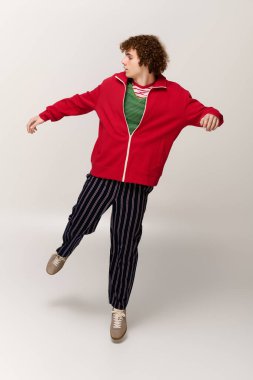 Hareketli genç kendine güvenen kırmızı ceket ve çizgili pantolonla poz veriyor, gençlik enerjisi yayıyor..