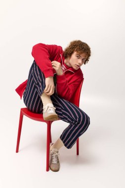 Benzersiz moda anlayışını canlı kırmızı bir sandalyede sergileyen genç çocuk..