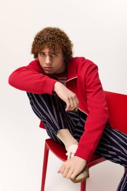 Kıvırcık saçlı genç çocuk canlı bir kıyafet giymiş, çağdaş moda eğilimlerini somutlaştırıyor..