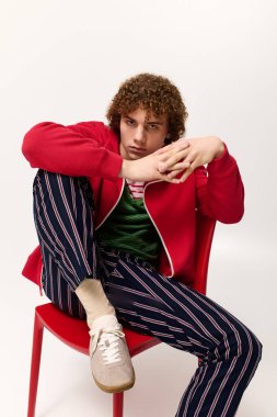 Şık bir genç, kendine güvenen bir poz veriyor. Parlak bir arka planda canlı bir kıyafet giyiyor..