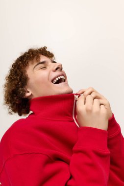 Havalı giyinmiş enerjik bir çocuk süveter yakasını şık bir şekilde yukarı çekerken gülüyor..