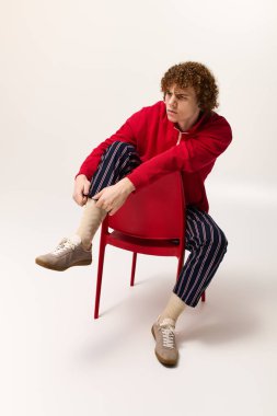 Çocuk benzersiz stilini modern bir ortamda parlak kırmızı bir sandalyede otururken gösteriyor..