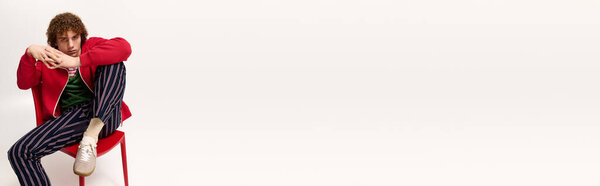 Уверенный подросток демонстрирует современную моду, позируя на красном стуле.