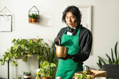 Genç bir Asyalı çiçekçi ustalıkla yeşilliklerle dolu parlak ve neşeli bir dükkanda bitkiler düzenliyor..
