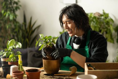 Genç bir çiçekçi özenle yemyeşil bir bitki yetiştirirken parlak renkler odayı dolduruyor..