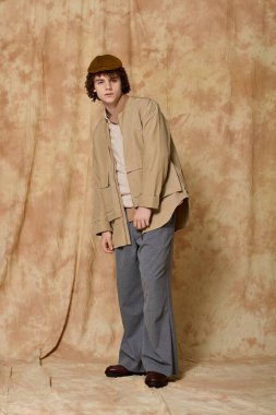 Kendine güvenen genç adam, yaratıcı bir ortamda eşsiz bir şapkayla şık giysilerini sergiliyor..