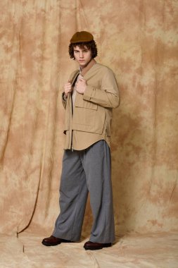 Yakışıklı genç, sıcak, desenli bir zemin karşısında kendine güvenen, modaya uygun katmanlar giymiş bir şekilde duruyor..