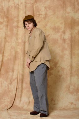 Yakışıklı genç rahat bir stüdyoda rahat bir şekilde poz veriyor, yumuşak ışık altında modaya uygun kıyafetler giyiyor..