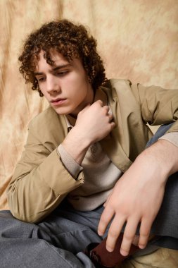 Tarz sahibi bir genç, düşünceli bir ifadeyle oturur, kapalı mekanda modaya uygun bir hava yaratır..