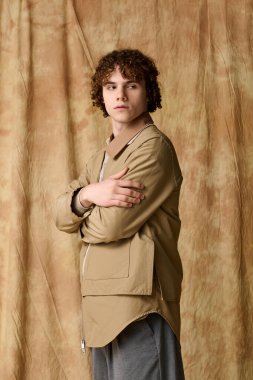 Yakışıklı genç kendine güvenerek duruyor, modaya uygun giyinmiş, yumuşak, altın bir zemin üzerinde.