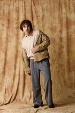 Yakışıklı bir genç, kendine güvenen bir şekilde şık kıyafetler içinde dokulu bir arka plana karşı poz verir..