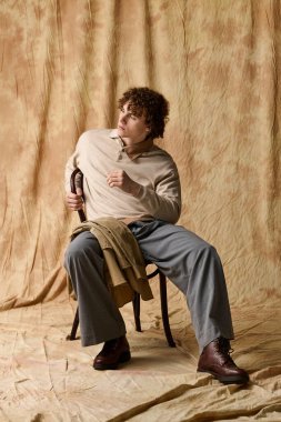 Şık bir genç zarif bir şekilde bir sandalyede oturur, büyüleyici ve kendine güvenir..