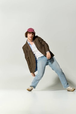 Moda kıyafetleri giymiş genç bir çocuk hafif eğilirken eğlenceli ve kendinden emin bir poz veriyor..