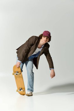 Şık giyinmiş yakışıklı bir genç stüdyoda kaykay tutarken eğiliyor..
