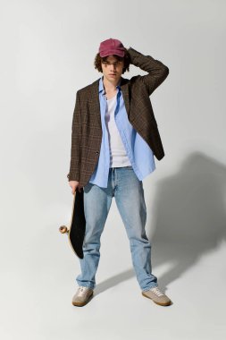 Spor ceketli ve günlük kıyafetli yakışıklı genç, kapalı alanda kaykayla rahatça poz veriyor.