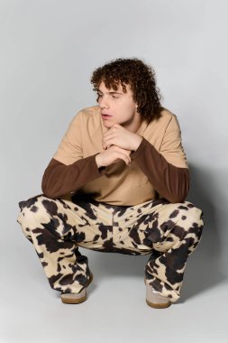 Tarz sahibi gençler, tarafsız bir arkaplan karşısında düşünceli bir şekilde çömeliyor..