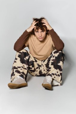 Yakışıklı genç elleri saçında yerde oturuyor, benzersiz bir moda ve tavır sergiliyor..