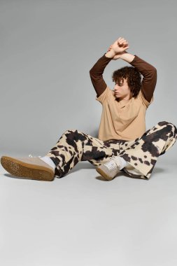 Yakışıklı genç stüdyo zemininde yaratıcı bir şekilde poz veriyor, modaya uygun kıyafetler ve rahat bir hava sergiliyor..