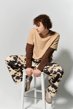 Kendinden emin genç bir adam, bir taburede otururken modern, modaya uygun bir stil sergiliyor..