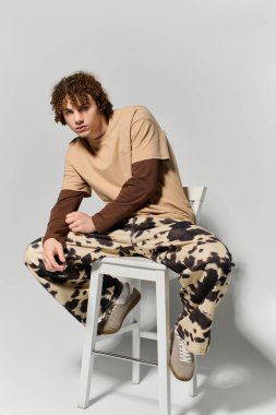 Şık bir genç, sıradan bir şekilde bir taburede oturur ve özel bir kıyafeti sergiler..