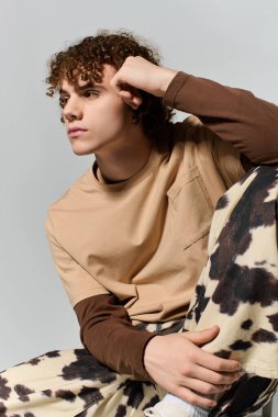 Yakışıklı bir genç, düşünceli bir ifadeyle oturur, minimalist bir ortamda şık bir kıyafet giyer..