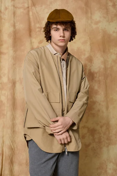 Yakışıklı genç kendine güvenerek poz veriyor, modaya uygun şekilde giyiniyor, desenli bir arka plana karşı..