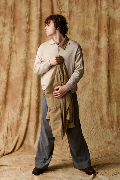 Yakışıklı genç, kendine güvenen, kumaşı tutan, dokusu sıcacık bir arka planla çevrili duruyor..