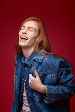 Uzun saçlı bir insan canlı kırmızı bir arka plana gülüyor, mutluluk saçıyor..